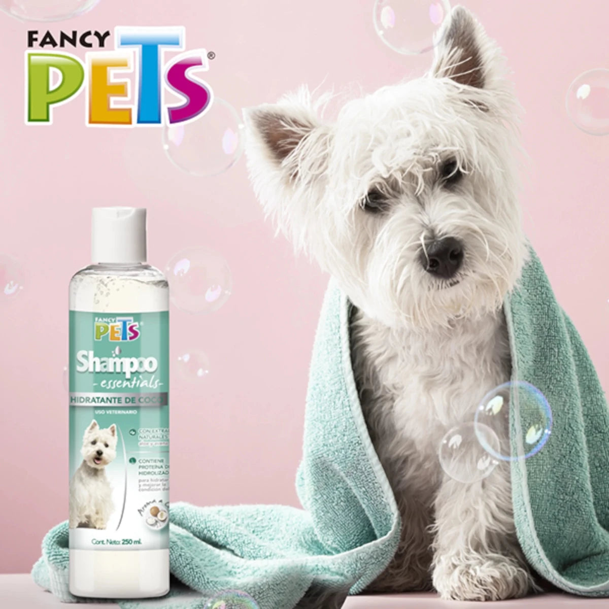 Perro blanco recién bañado envuelto en toalla junto a la botella de Shampoo Essentials Hidratante de Coco Fancy Pets, ideal para hidratar la piel y dar brillo al pelaje.
