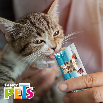 Un gatito siendo cargado cariñosamente por su dueño mientras lame felizmente el premio cremoso Yummy Creamy sabor atún y salmón directamente del tubo, en Kamalitas.