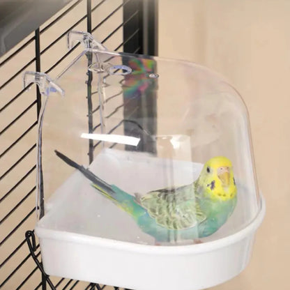 Bañera exterior transparente con base blanca para canarios y periquitos, colgada en la jaula con un ave bañándose dentro.